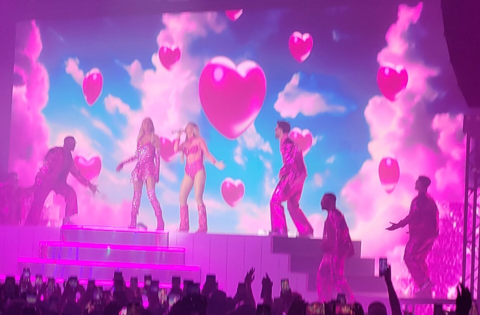 Concert performers in pink, hearts backdrop.