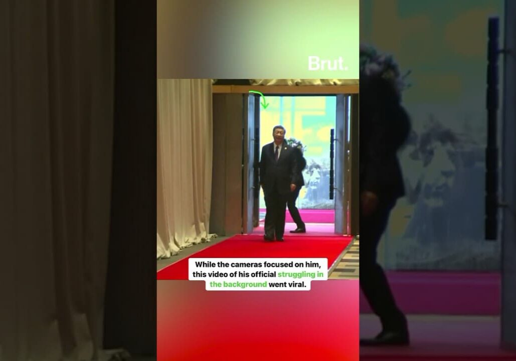 Man walking on red carpet, official struggling.